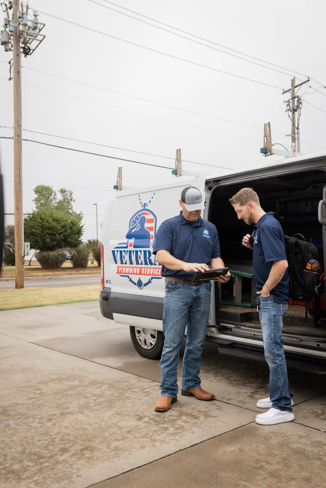 Veteran Plumbing Services technicians reviewing job details on a tablet beside a company van